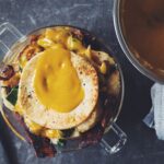 Close-up of a vegan biscuit, bacon, and egg breakfast trifle with a runny vegan egg yolk, showcasing a delicious and innovative food breakfast option.