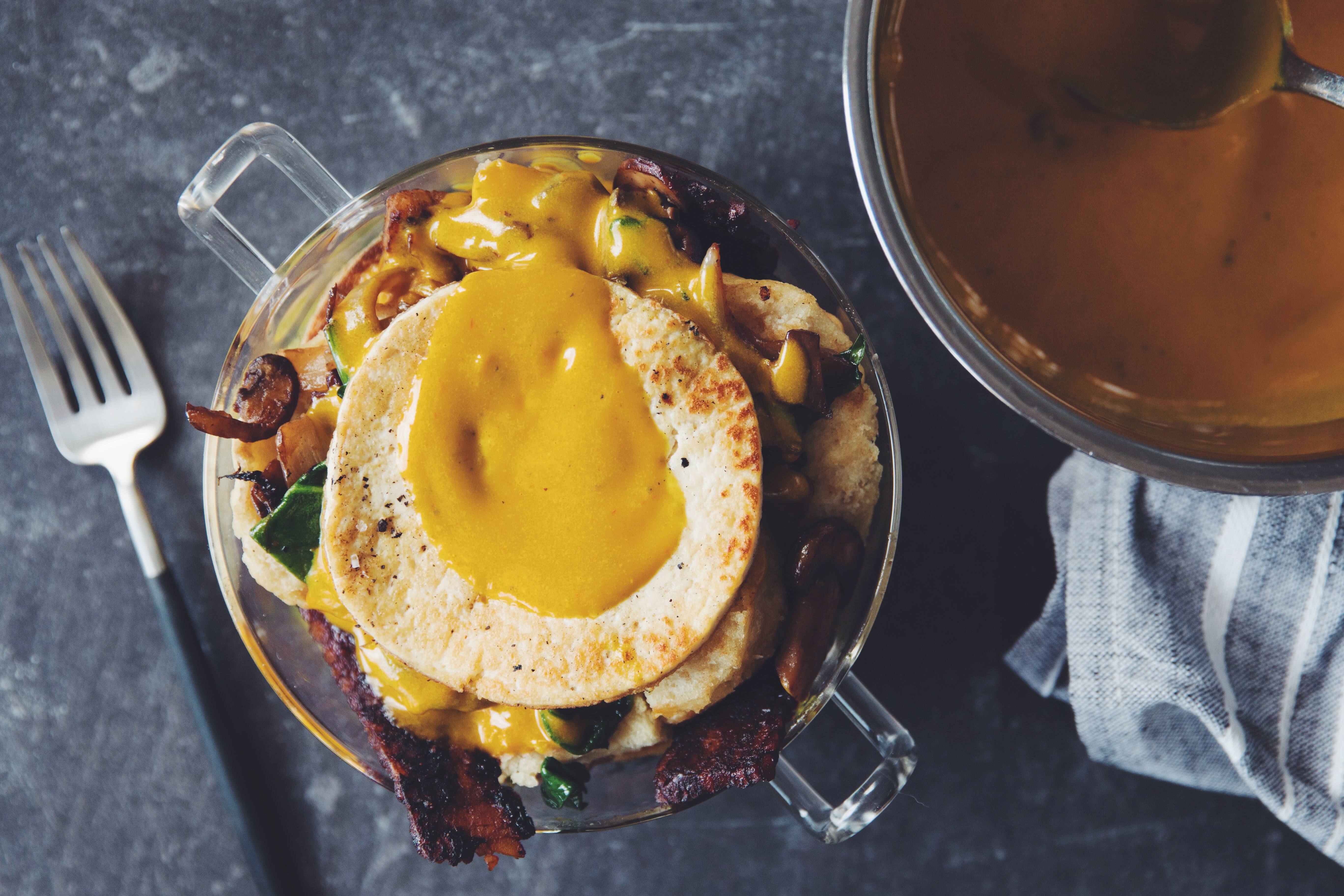 Close-up of a vegan biscuit, bacon, and egg breakfast trifle with a runny vegan egg yolk, showcasing a delicious and innovative food breakfast option.