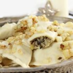 Close-up of boiled pierogi topped with fried onions and herbs, showcasing their crescent shape and inviting filling.