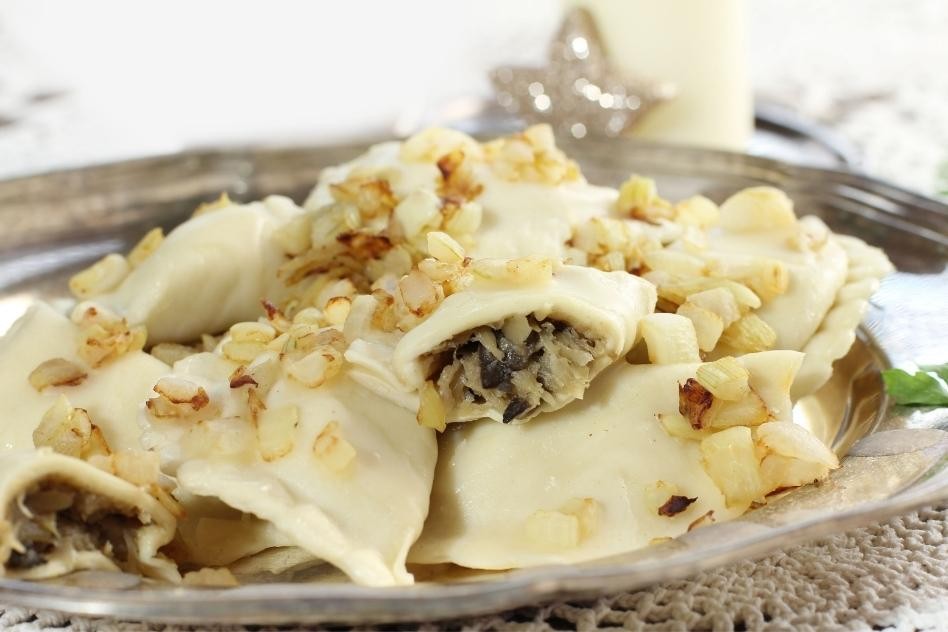 Close-up of boiled pierogi topped with fried onions and herbs, showcasing their crescent shape and inviting filling.