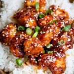 Close up of Crispy Sesame Chicken with a sticky Asian sauce served over rice, highlighting the delicious texture and vibrant colors.