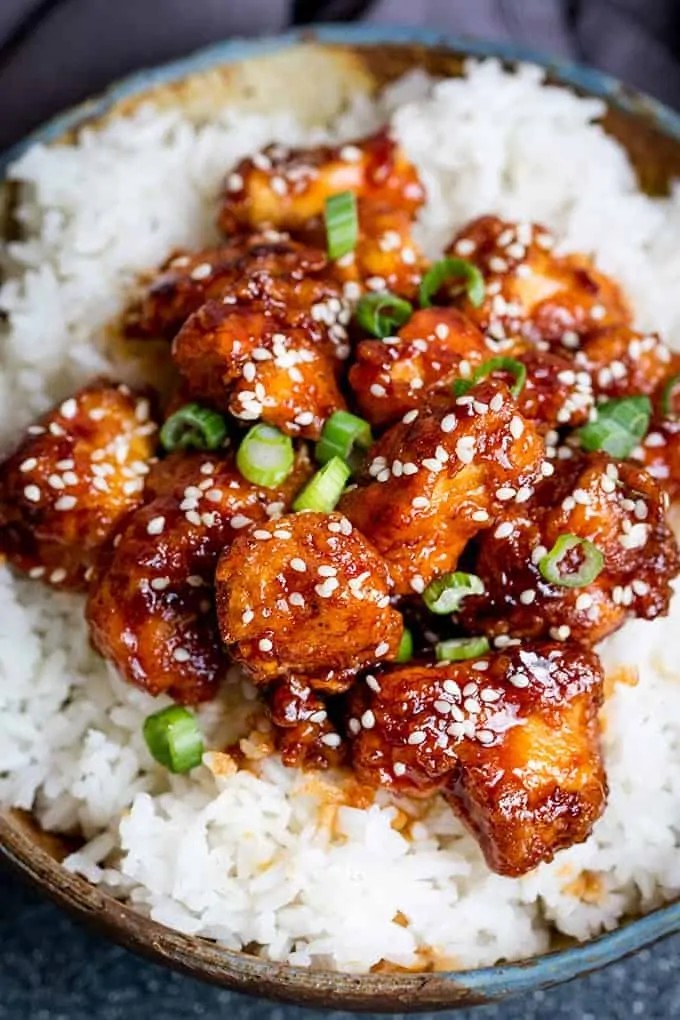 Close up of Crispy Sesame Chicken with a sticky Asian sauce served over rice, highlighting the delicious texture and vibrant colors.