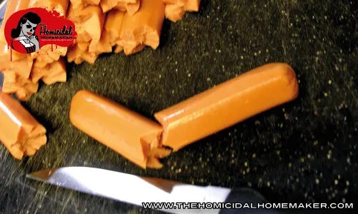 Close-up of hot dogs being partially sliced at an angle to create a ripped flesh effect for zombie finger food appetizers.