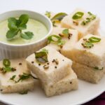 Close-up of White Dhokla, a steamed and fermented Gujarati snack, garnished with fresh coriander and served in square pieces.