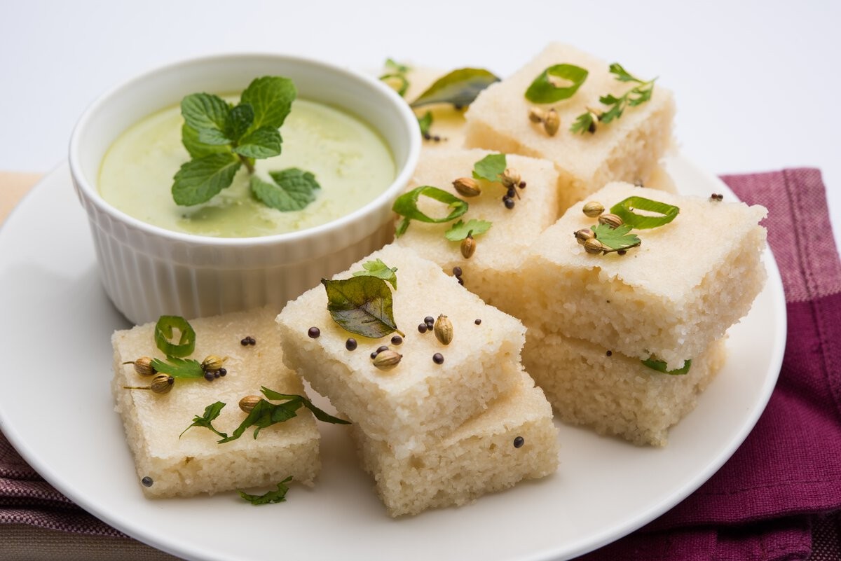 Close-up of White Dhokla, a steamed and fermented Gujarati snack, garnished with fresh coriander and served in square pieces.