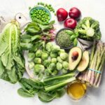 Colorful array of vitamin K rich foods including leafy greens, broccoli, and berries on a white background