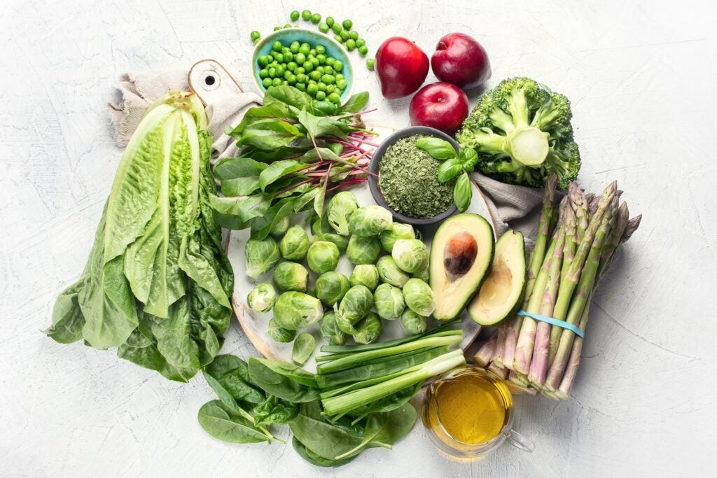 Colorful array of vitamin K rich foods including leafy greens, broccoli, and berries on a white background