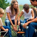 Family enjoying a camping meal of beans and sausages around a campfire