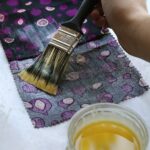 Hand with brush applying golden substance to decorative cloth for DIY beeswax food wrap