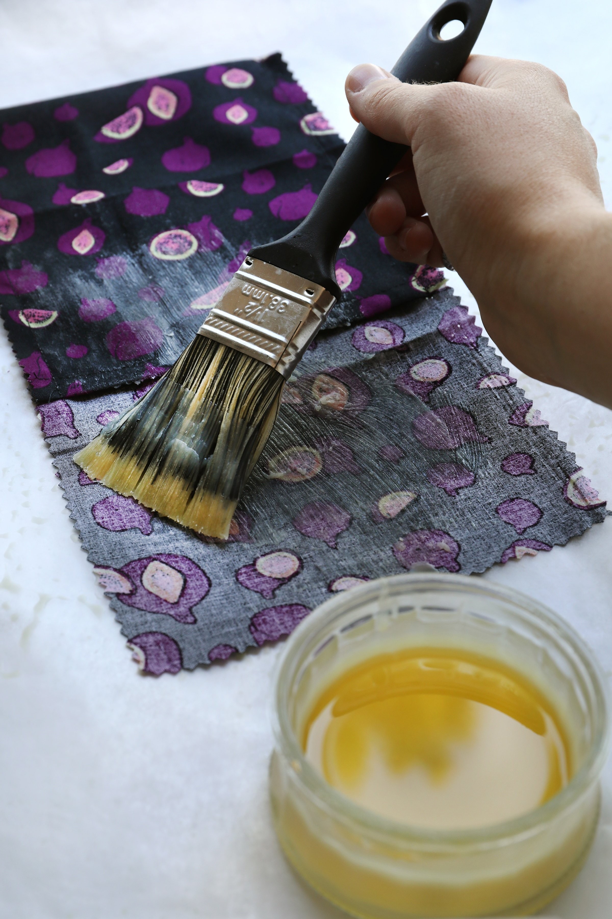 Hand with brush applying golden substance to decorative cloth for DIY beeswax food wrap