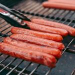 Hot dogs sizzling on a barbecue grill.