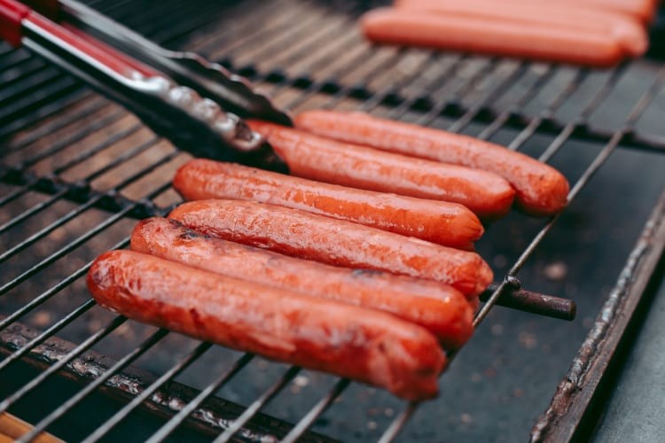 Hot dogs sizzling on a barbecue grill.