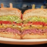 Houston's towering cheeseburger, a classic food restaurant burger, sliced in half and served with pickles and fries.