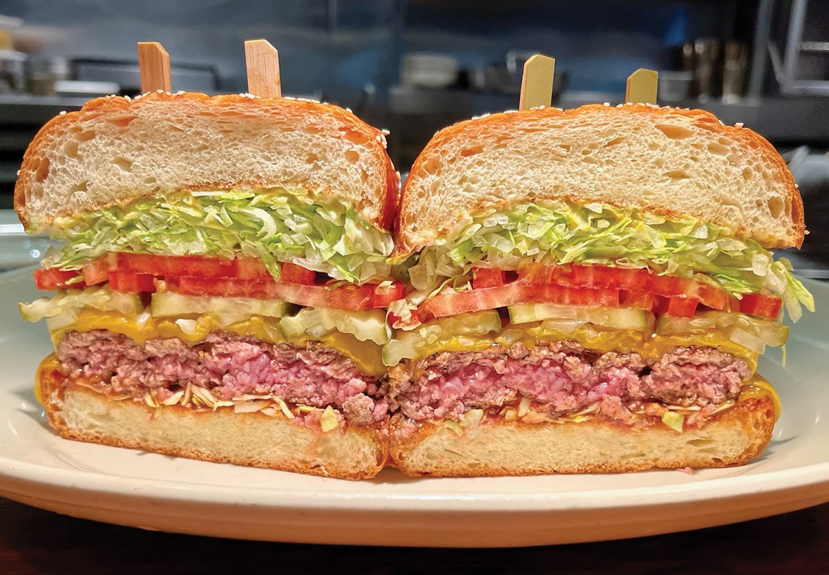 Houston's towering cheeseburger, a classic food restaurant burger, sliced in half and served with pickles and fries.