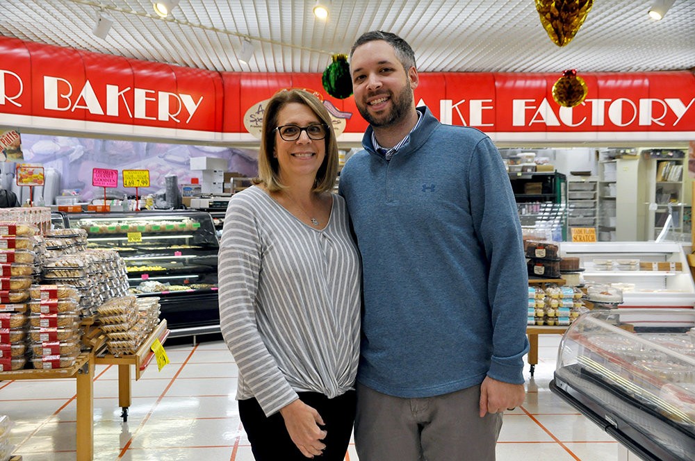 Joanne Greeley Graham and her son, Justin Graham, stand proudly in the bakery section of Geresbeck's Food Market in Pasadena, showcasing eclairs and marshmallow doughnuts.