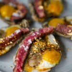 Overhead shot of the Billionaire's Breakfast featuring wagyu beef, oysters, and quail eggs, garnished with gold flakes, showcasing a luxurious and indulgent meal.