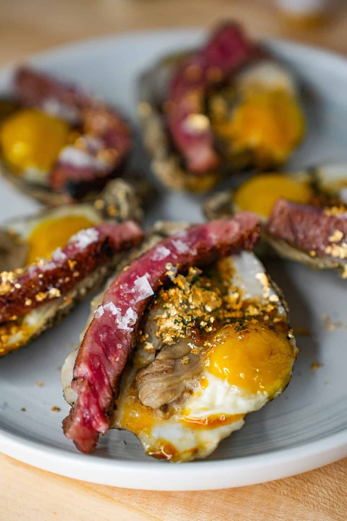 Overhead shot of the Billionaire's Breakfast featuring wagyu beef, oysters, and quail eggs, garnished with gold flakes, showcasing a luxurious and indulgent meal.