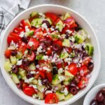 Overhead view of a vibrant Mediterranean Salad in a white bowl, showcasing fresh vegetables and a light dressing