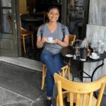 Photo of Antoinette sitting outside a coffee shop holding a cup of Greek coffee in Athens Greeece.