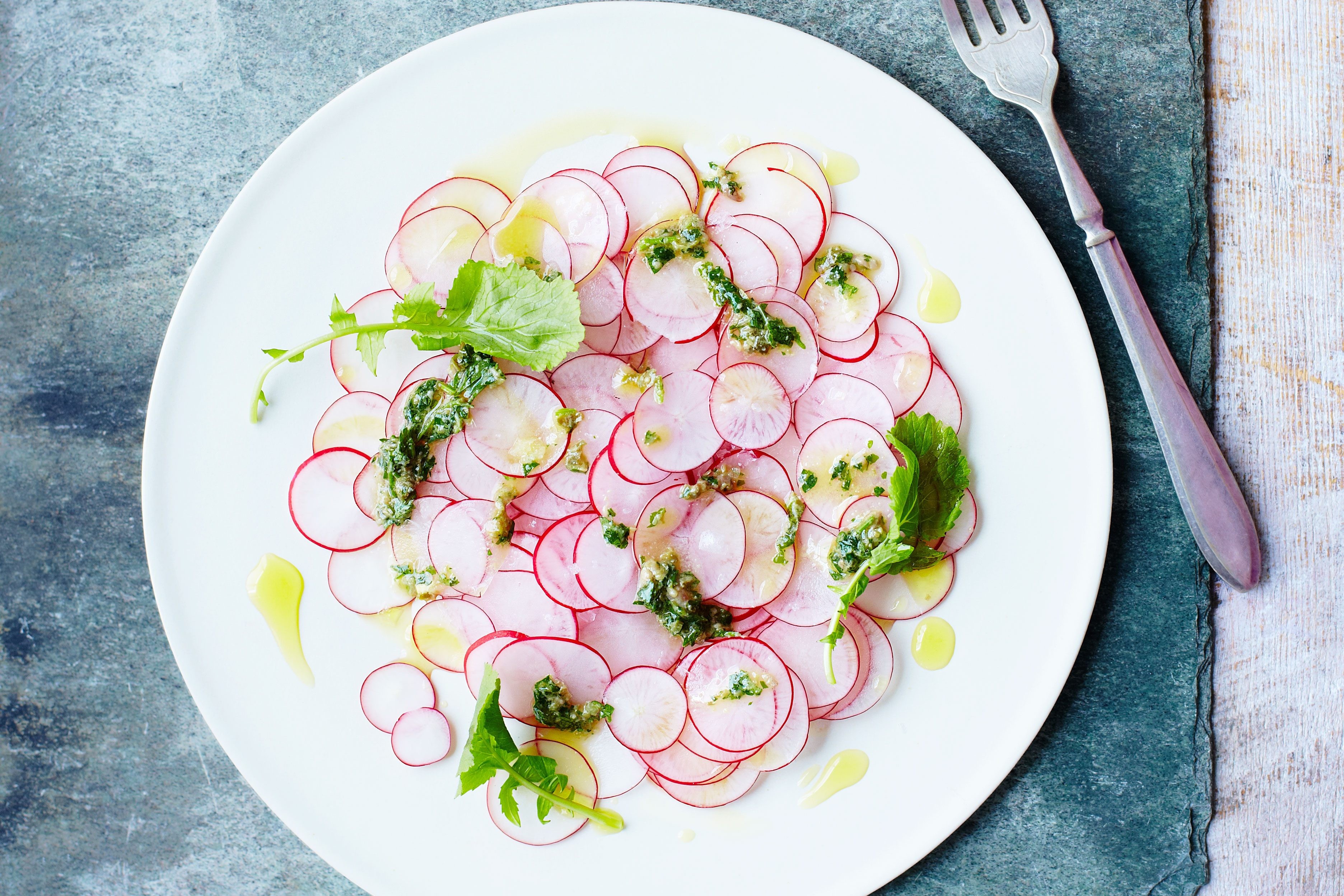 Plate of thinly sliced radishes with salsa verde dressing