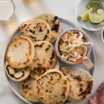 Pupusas on a round plate with curtido and limes