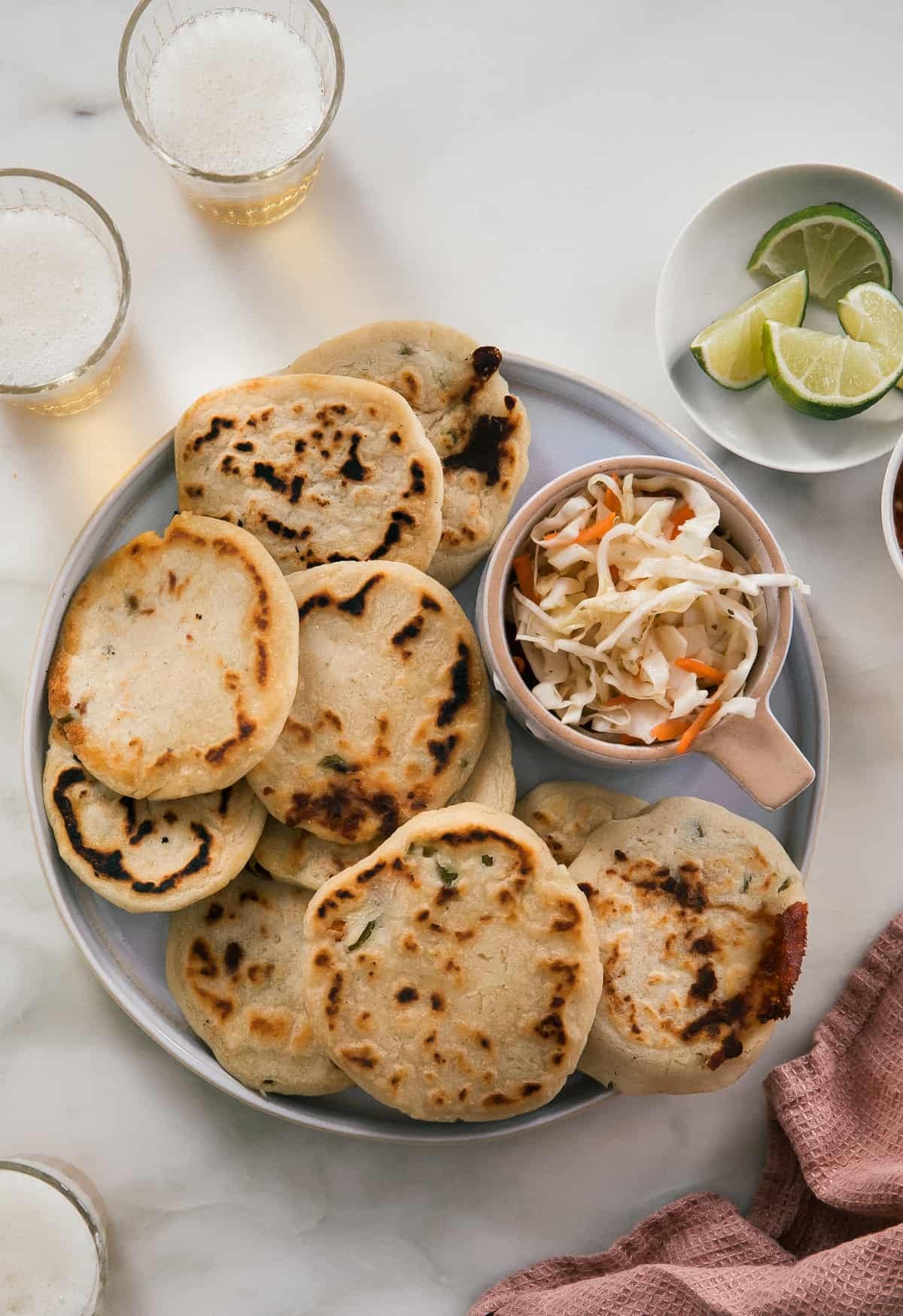 Pupusas on a round plate with curtido and limes