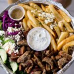 takeout container of Mediterranean food in Seattle: gyro meat, Greek fries, and salad.