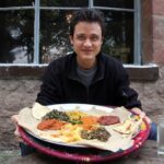 The author, Mark Wiens, pictured at a table laden with a colorful array of vegetarian Ethiopian dishes, ready to enjoy a plant-based feast.