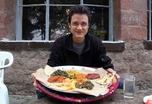 The author, Mark Wiens, pictured at a table laden with a colorful array of vegetarian Ethiopian dishes, ready to enjoy a plant-based feast.