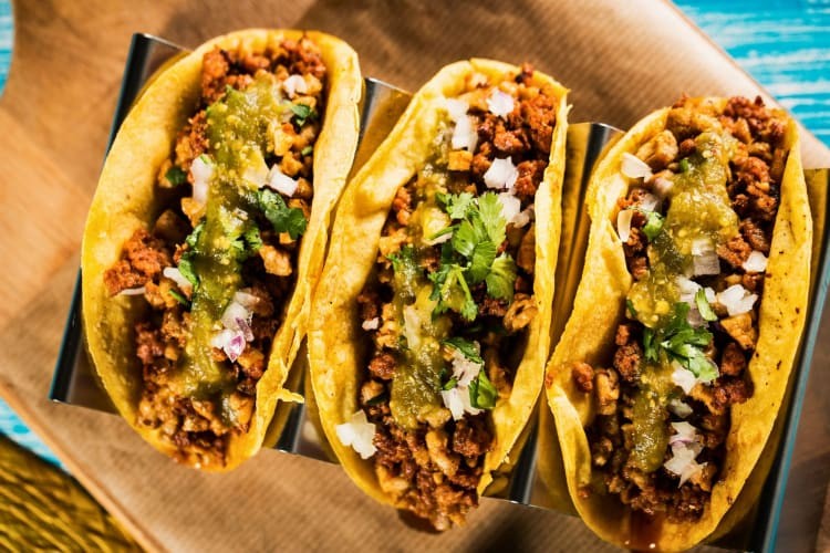 Three flavorful meat tacos garnished with fresh guacamole.