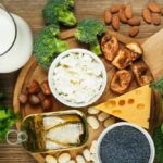 top view wooden board with various cheese, nuts, broccoli, canned fish, and jug of milk