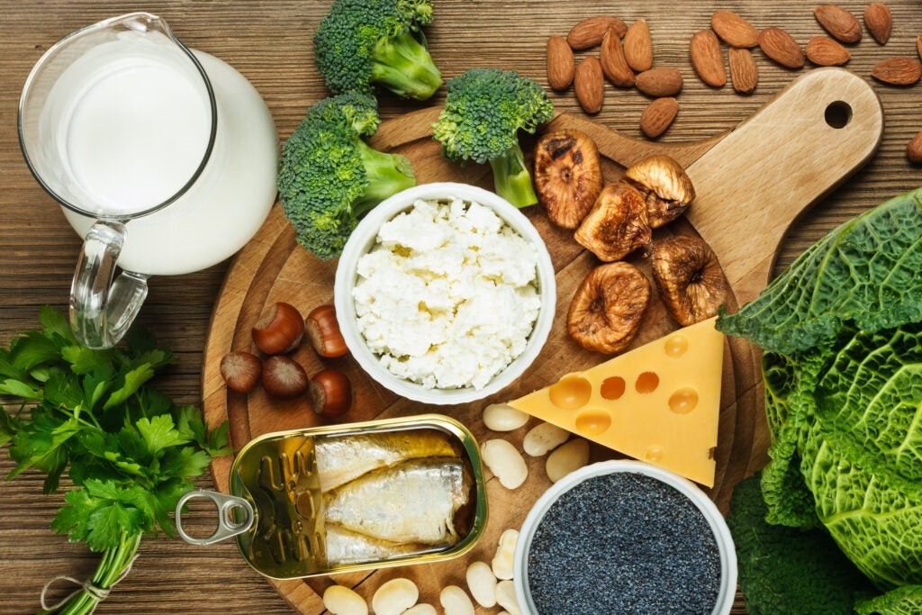 top view wooden board with various cheese, nuts, broccoli, canned fish, and jug of milk