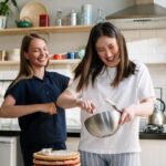 Two women laughing while making a cake, representing the enjoyment of occasional treats but also highlighting baked goods as potentially high in glucose.