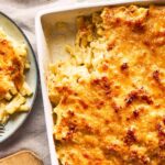 Macaroni and cheese in a white oven proof dish next to a plate with some of the macaroni cheese