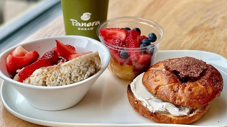 A bagel, fruit cup, oatmeal with strawberries, and drink from Panera, showcasing their limited breakfast hours
