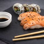 Close up of Japanese salmon sushi and a tuna avocado roll on a slate with soy sauce and chopsticks