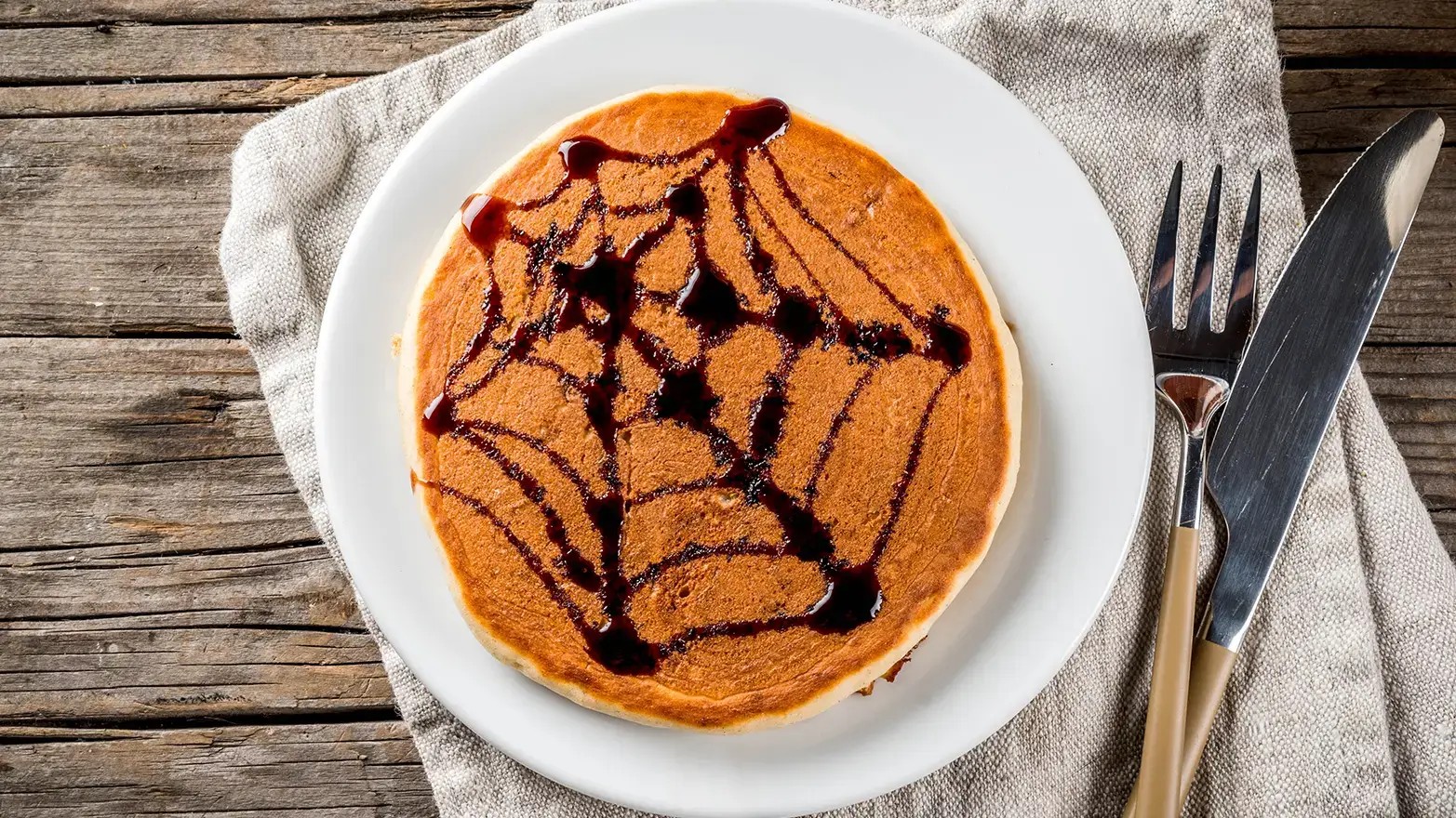 Pancakes decorated with red syrup spiderweb, perfect for a spooky Halloween brunch