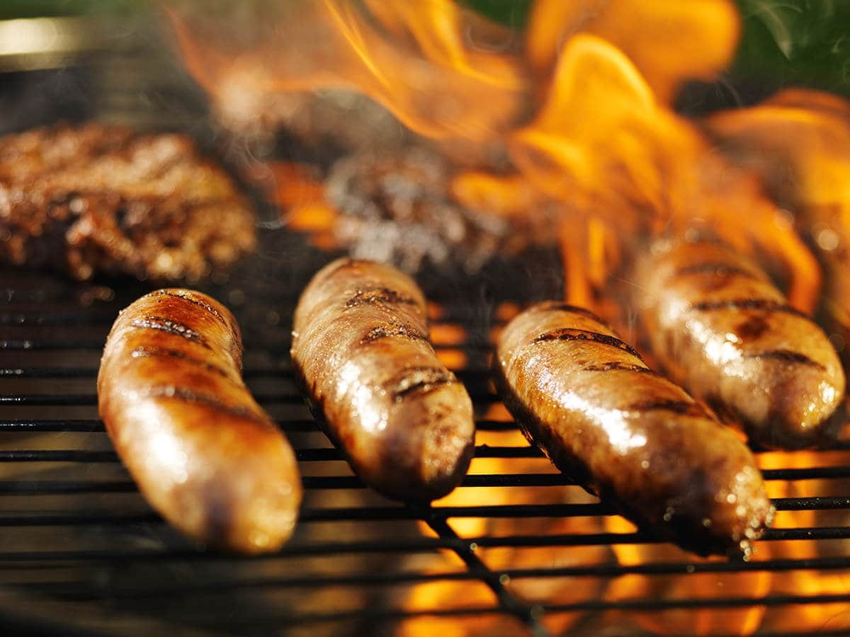 Brats sizzling on a grill alongside vibrant bell peppers and onions, creating a colorful and appetizing scene.
