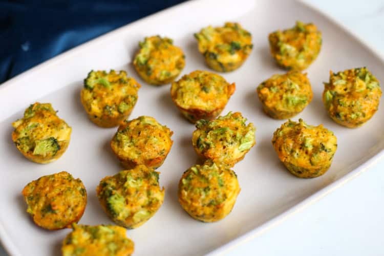 Broccoli cheddar bites lined up on a white serving platter.