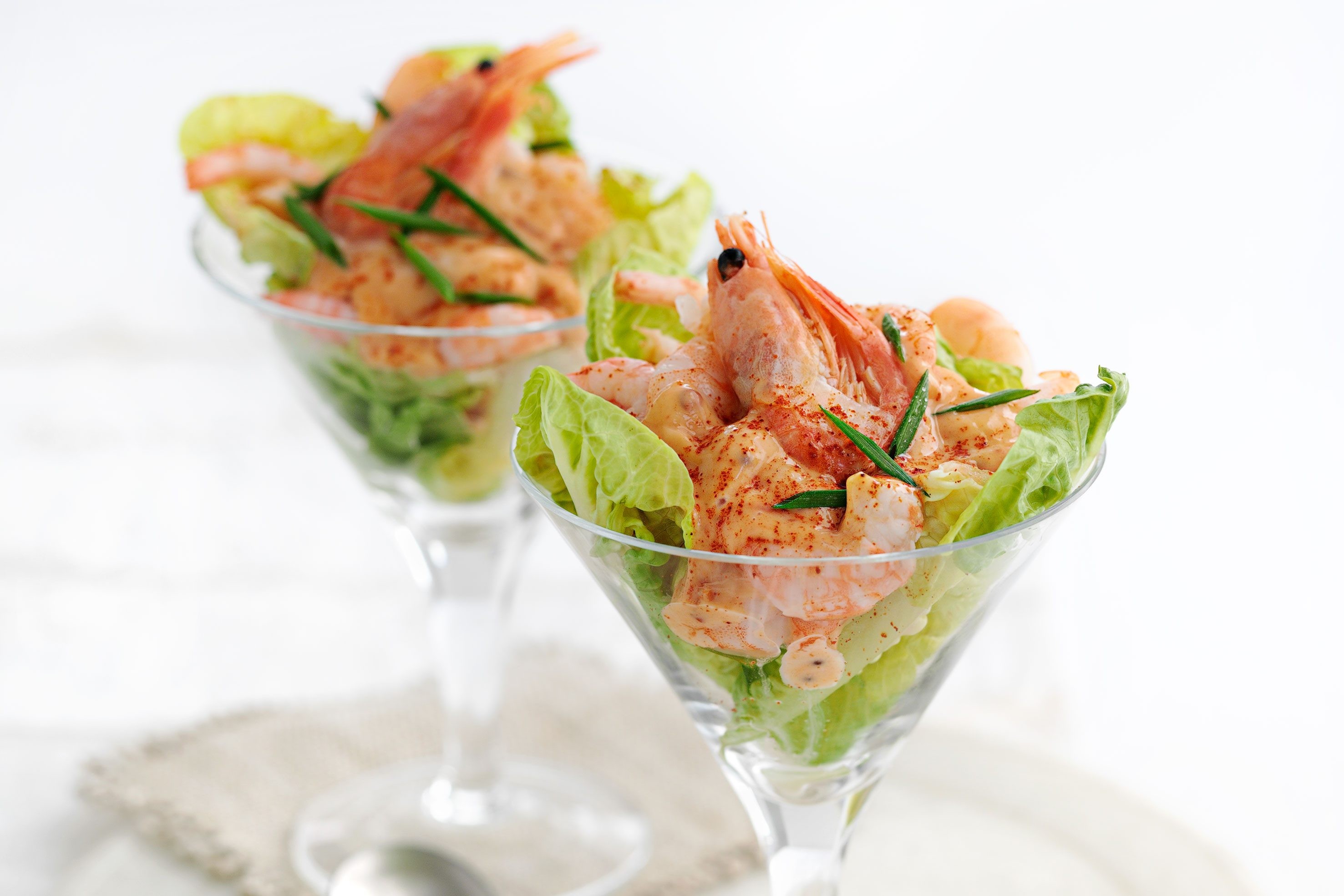 Two cocktail glasses filled with prawns, lettuce, avocado, mayonnaise and lemon. The glasses are filled with a prawn salad.