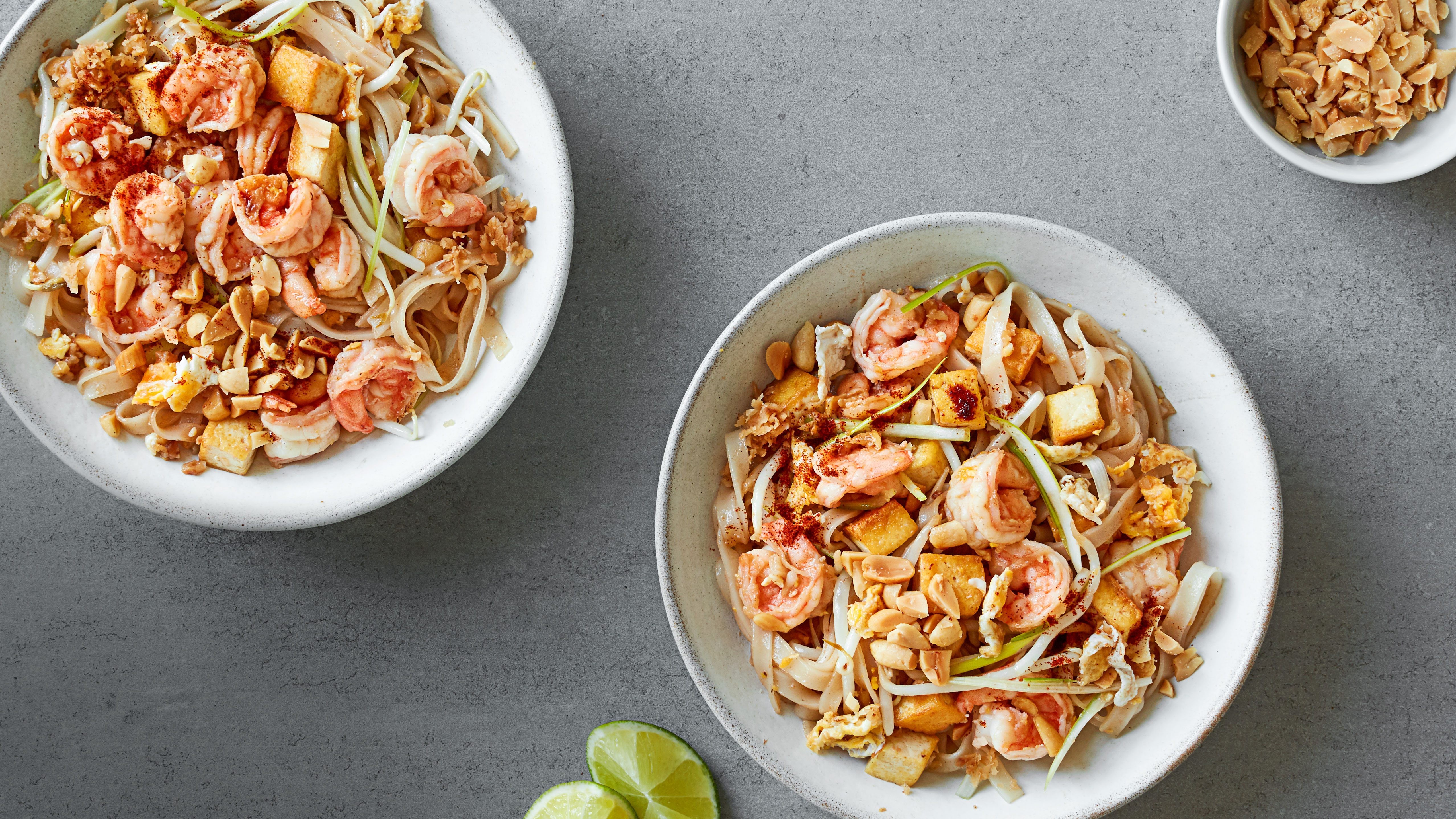 Authentic pad thai next to two wedges of lime and small bowl of peanuts