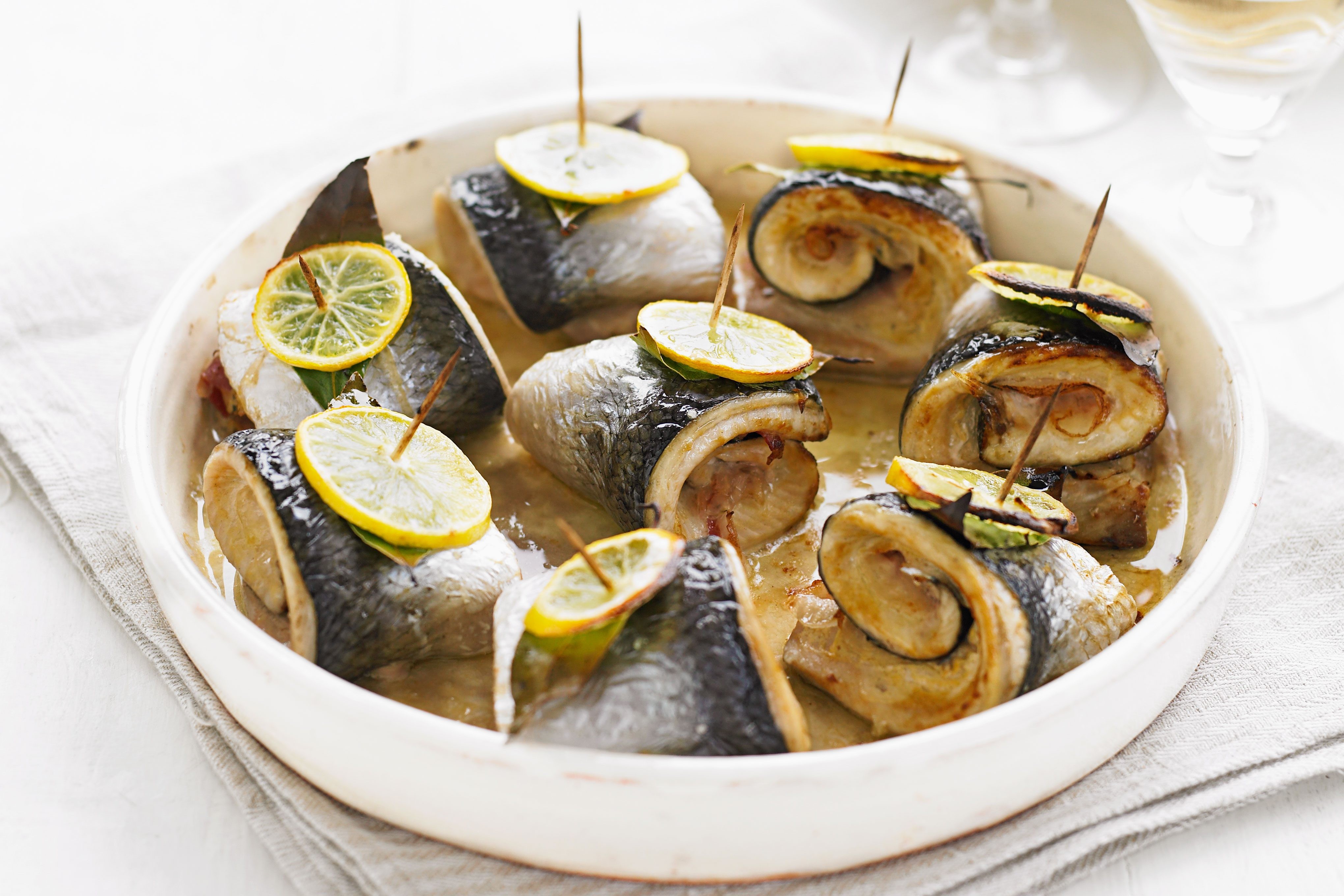 Bowl of skewered rolled herring with mustard and pancetta topped with lemon rounds. Bowl filled with rolled herring skewers.