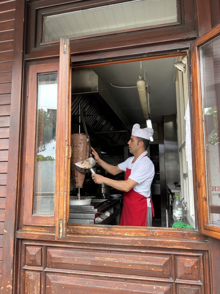 A close-up of Döner Kebab, slices of marinated meat being carved from a vertical spit at a street vendor