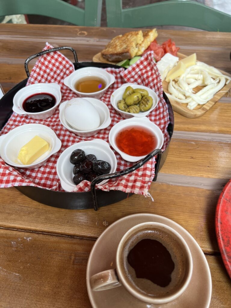 A spread of Turkish breakfast items, including olives, vegetables, cured meats, dips, eggs, fresh cheeses, baked bread, and fruit preserves