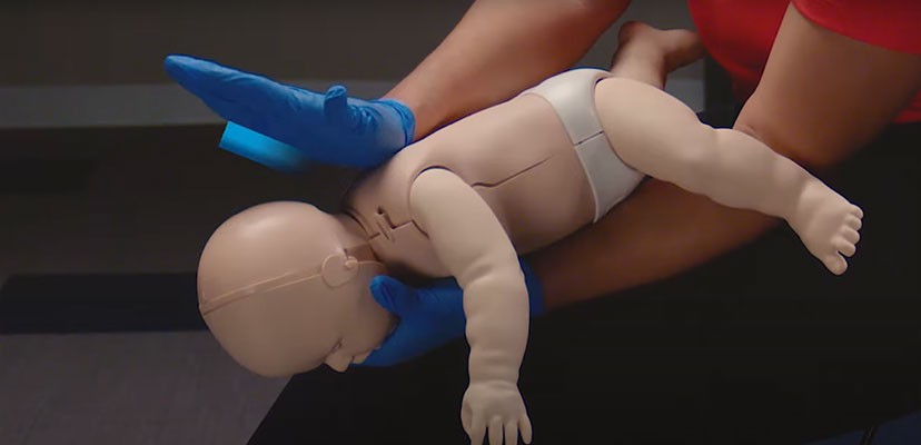 Adult demonstration of choking first aid on an infant manikin.
