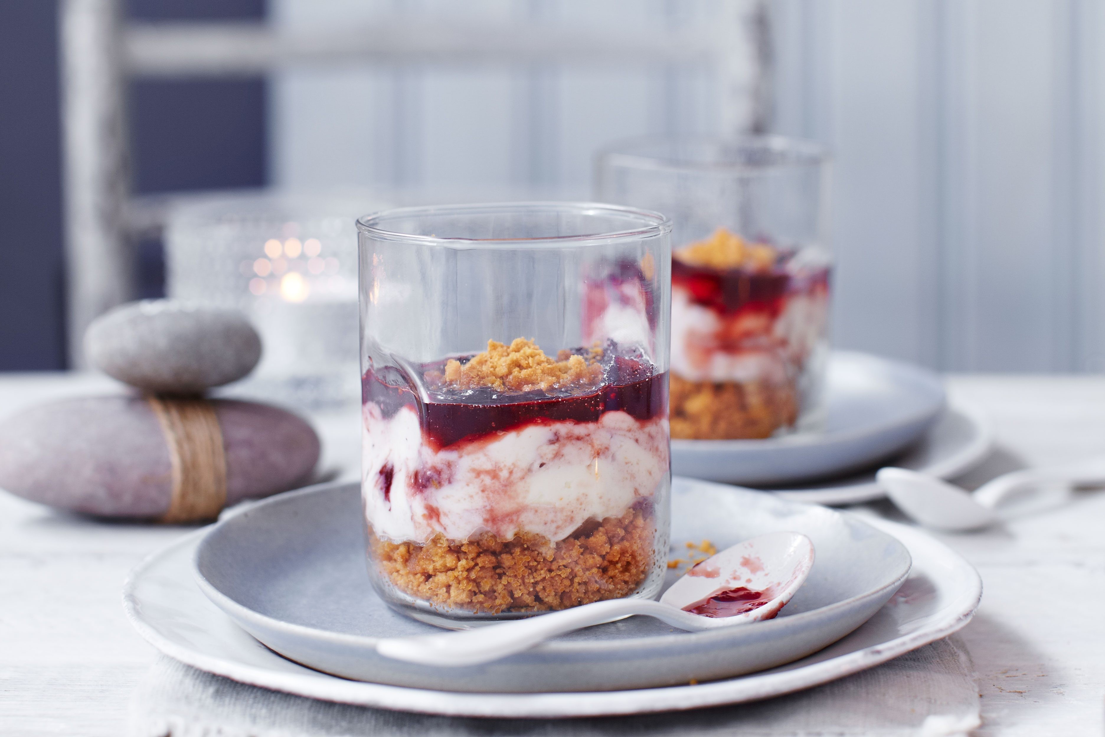 Two small glasses filled with lingonberry and ginger biscuit cheesecake. Two glasses filled with lingonberry cheesecake.