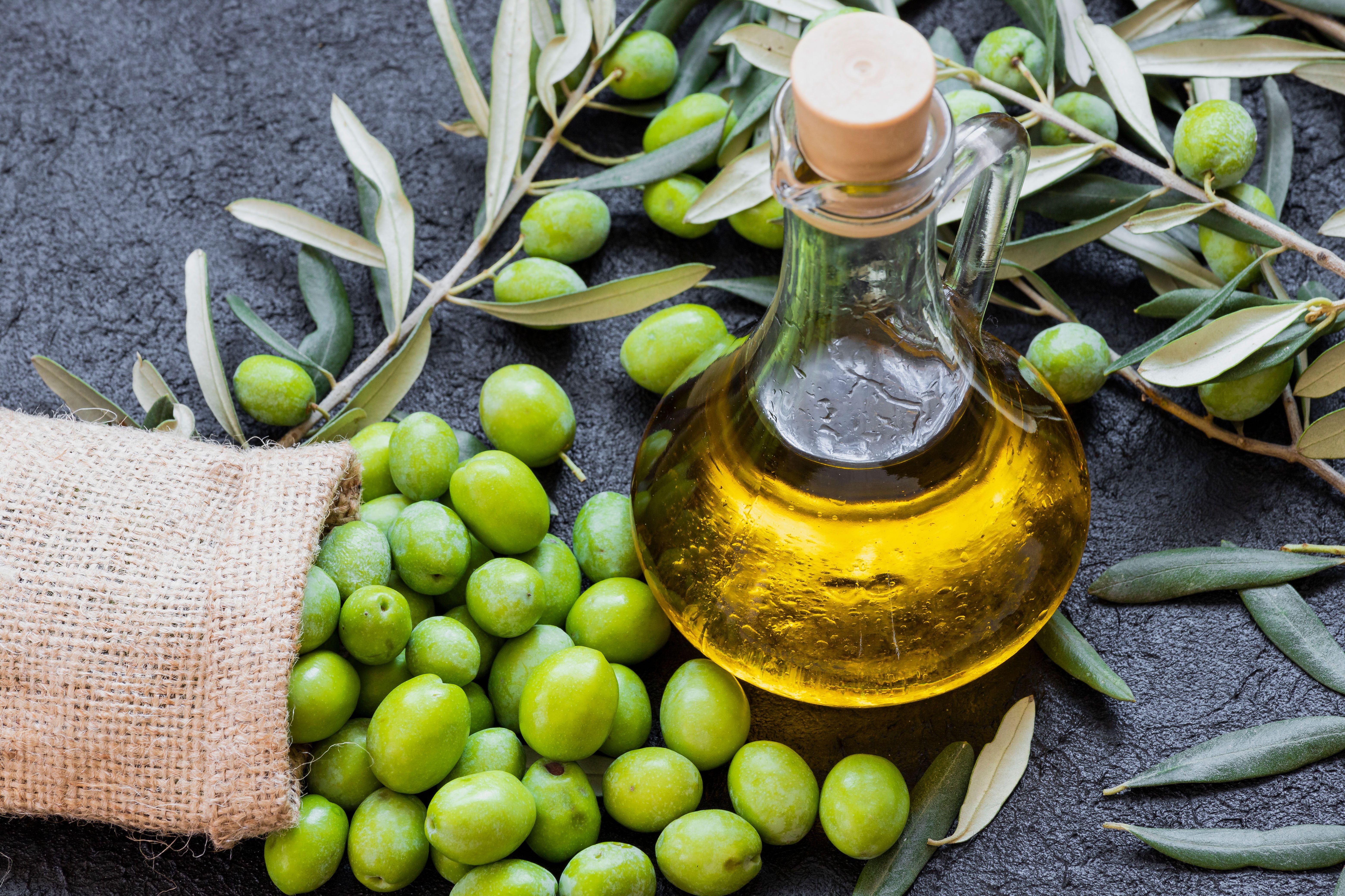 A bottle of olive oil next to fresh olives