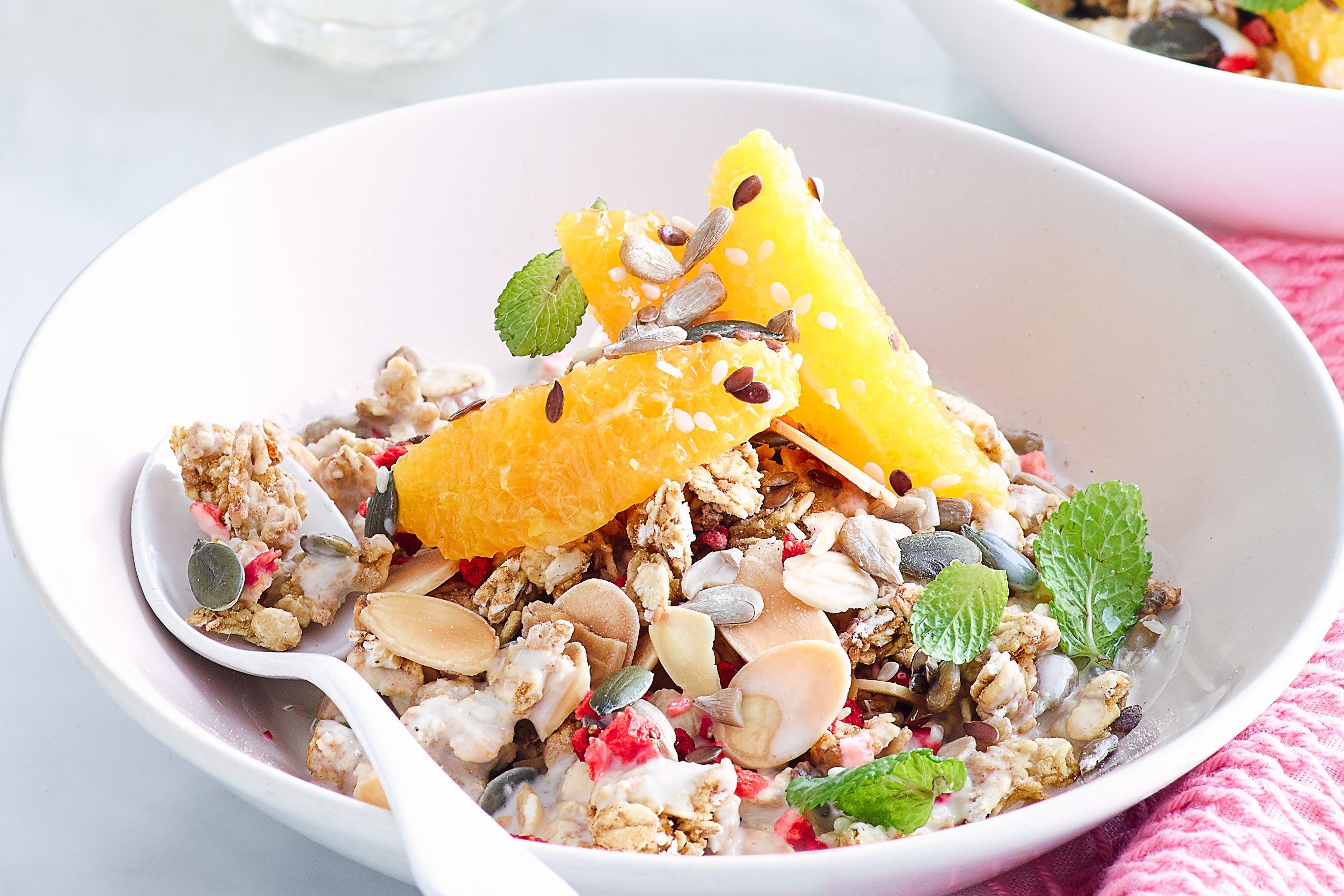 Bowl of granola with orange, raspberries and other nuts. The bowl is filled with granola, nuts, seeds and fruit.