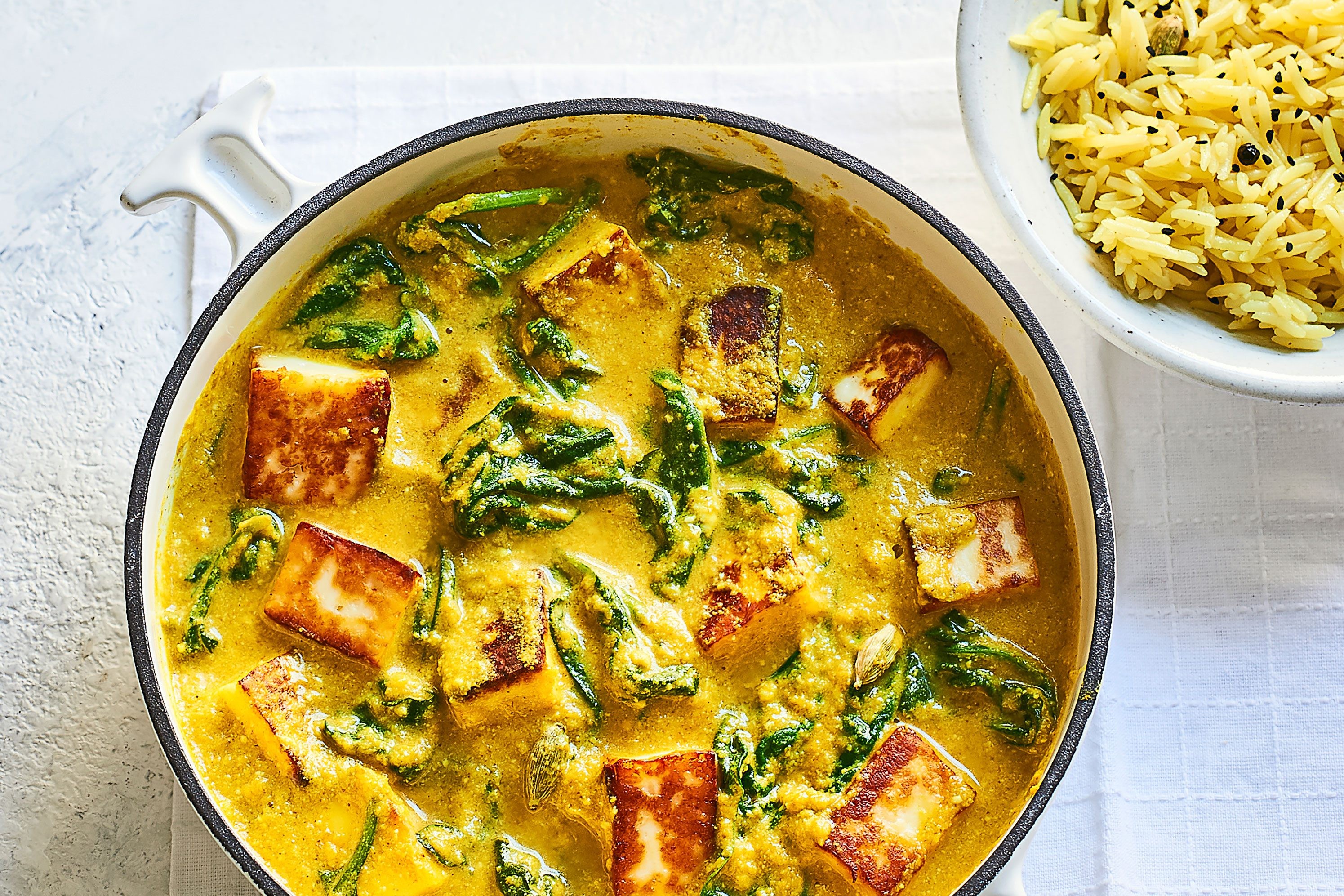 Panner korma in a large pot next to a bowl of rice