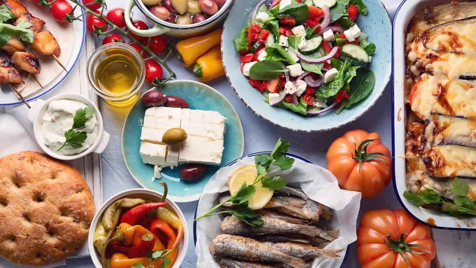 A spread of Greek food, including moussaka, meze, souvlaki, fish, pita, Greek salad, tzatziki, olives, and vegetables, showcasing the diversity and freshness of Greek cuisine